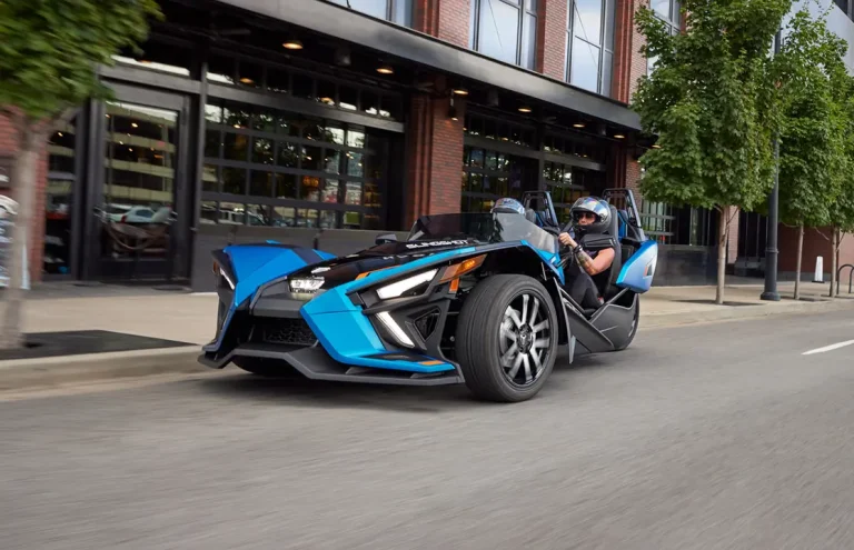 A blue and black three-wheeled vehicle driving on an urban street.
